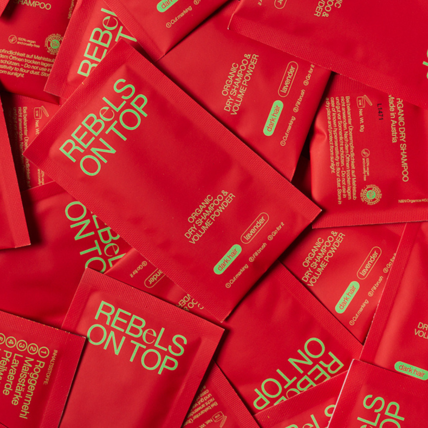 Viele Bio-Trockenshampoo-Nachfüllpäckchen in Rot für dunkles Haar, wild durcheinander auf einem Haufen liegend