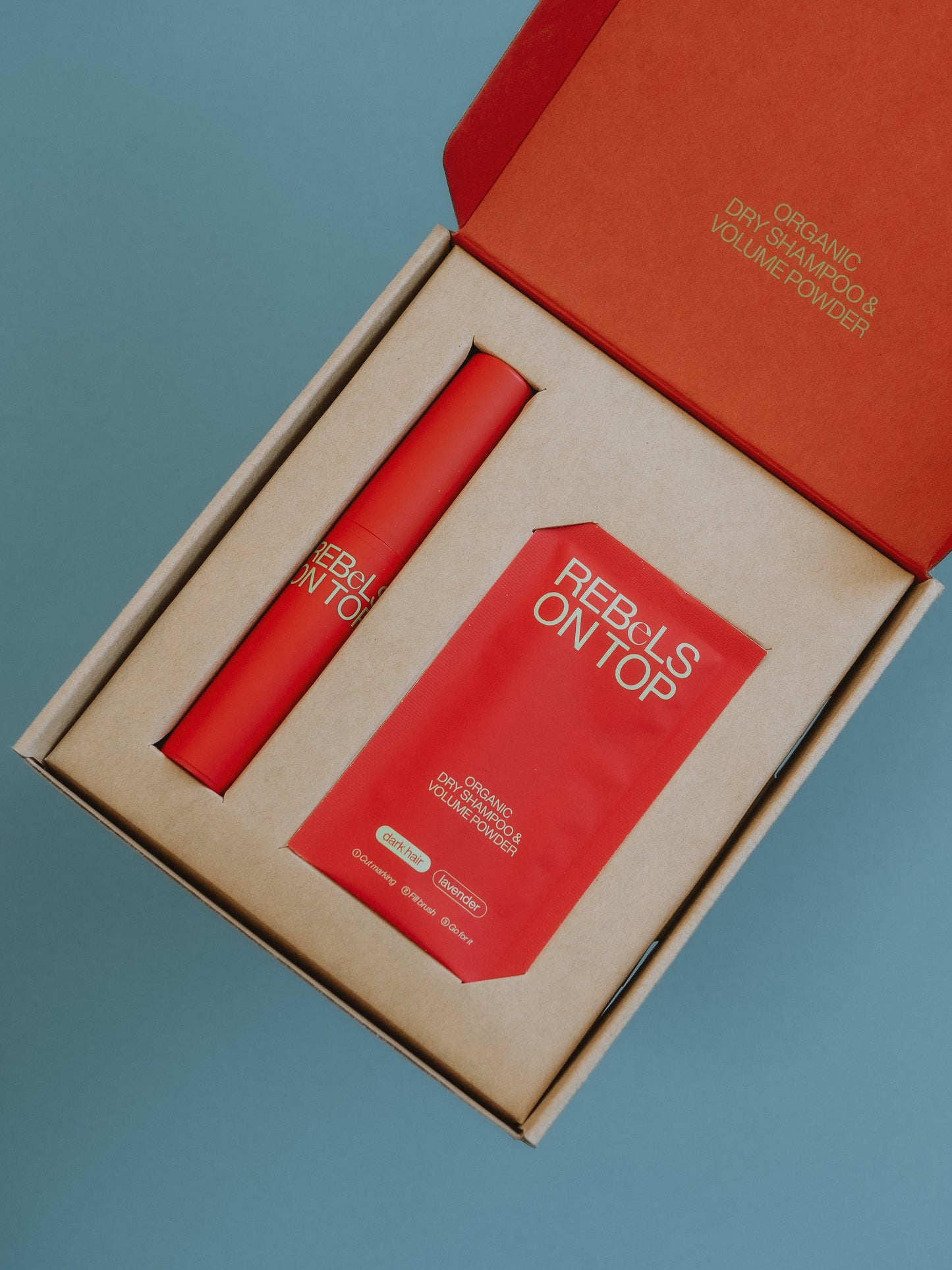 Geöffnetes Bio-Trockenshampoo-Starterkit mit nachfüllbarem Pinsel und einem Nachfüllpäckchen in Rot für dunkles Haar